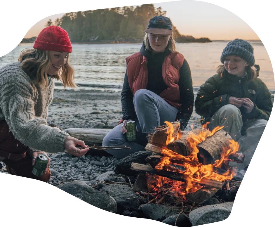 Three women sitting around a campfire on a rocky beach near the water