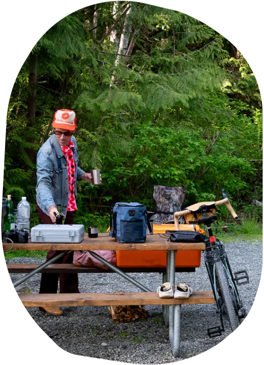 Man picking up cooking ware off of picnic table at campground with his bike nearby