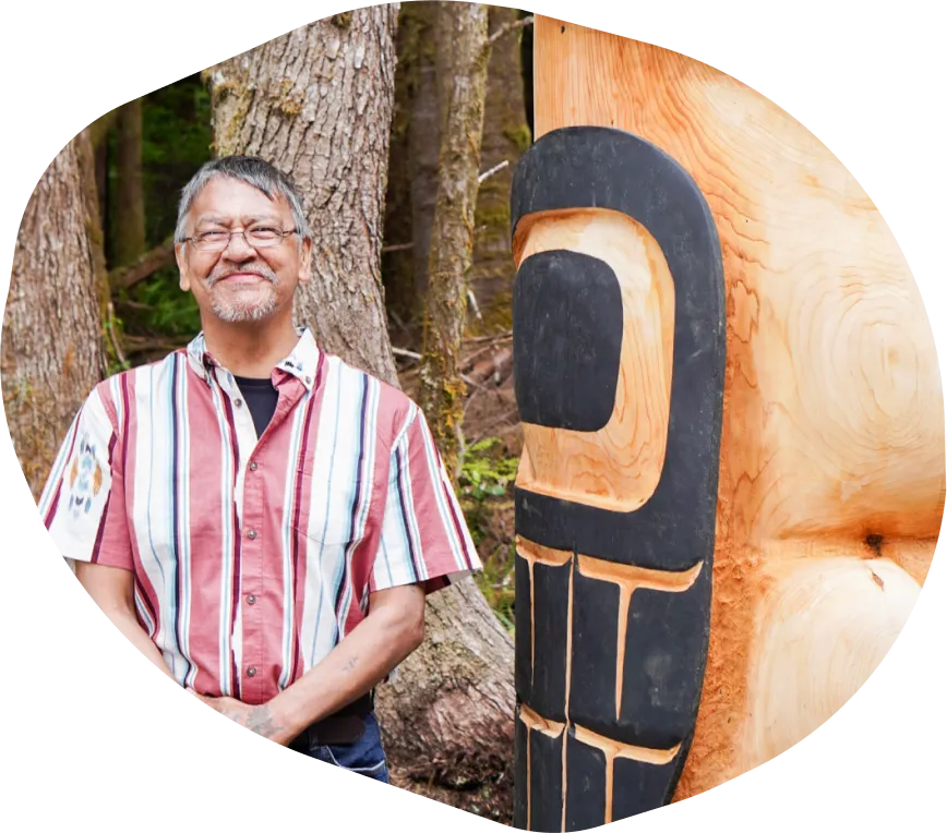 A man standing next to a large carved totem pole